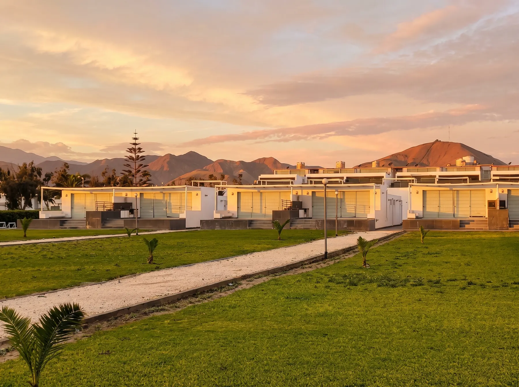 Condominio al atardecer con jardines, palmeras y cerros