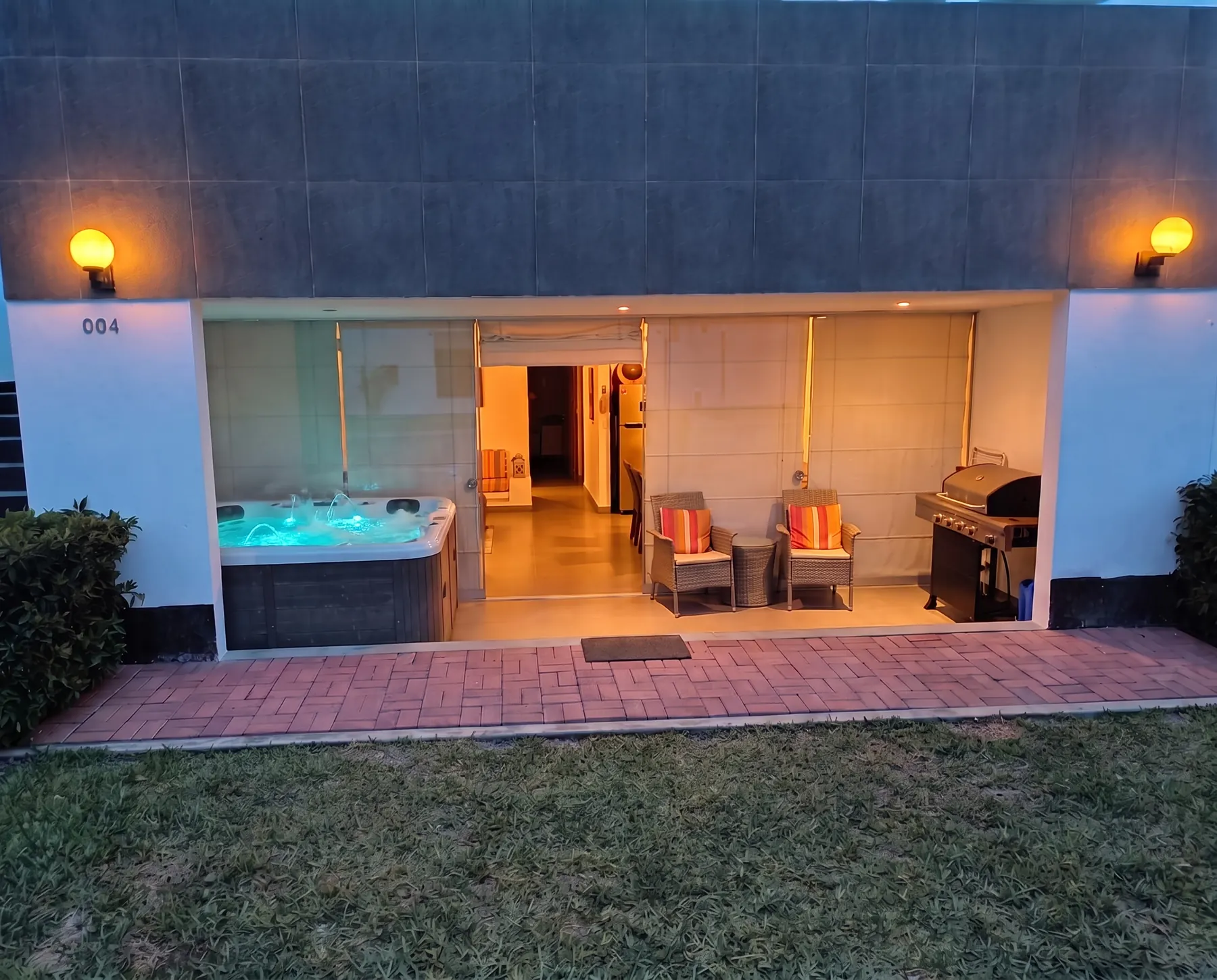 Fachada del depa de noche: faroles encendidos, interior iluminado y jacuzzi con luz