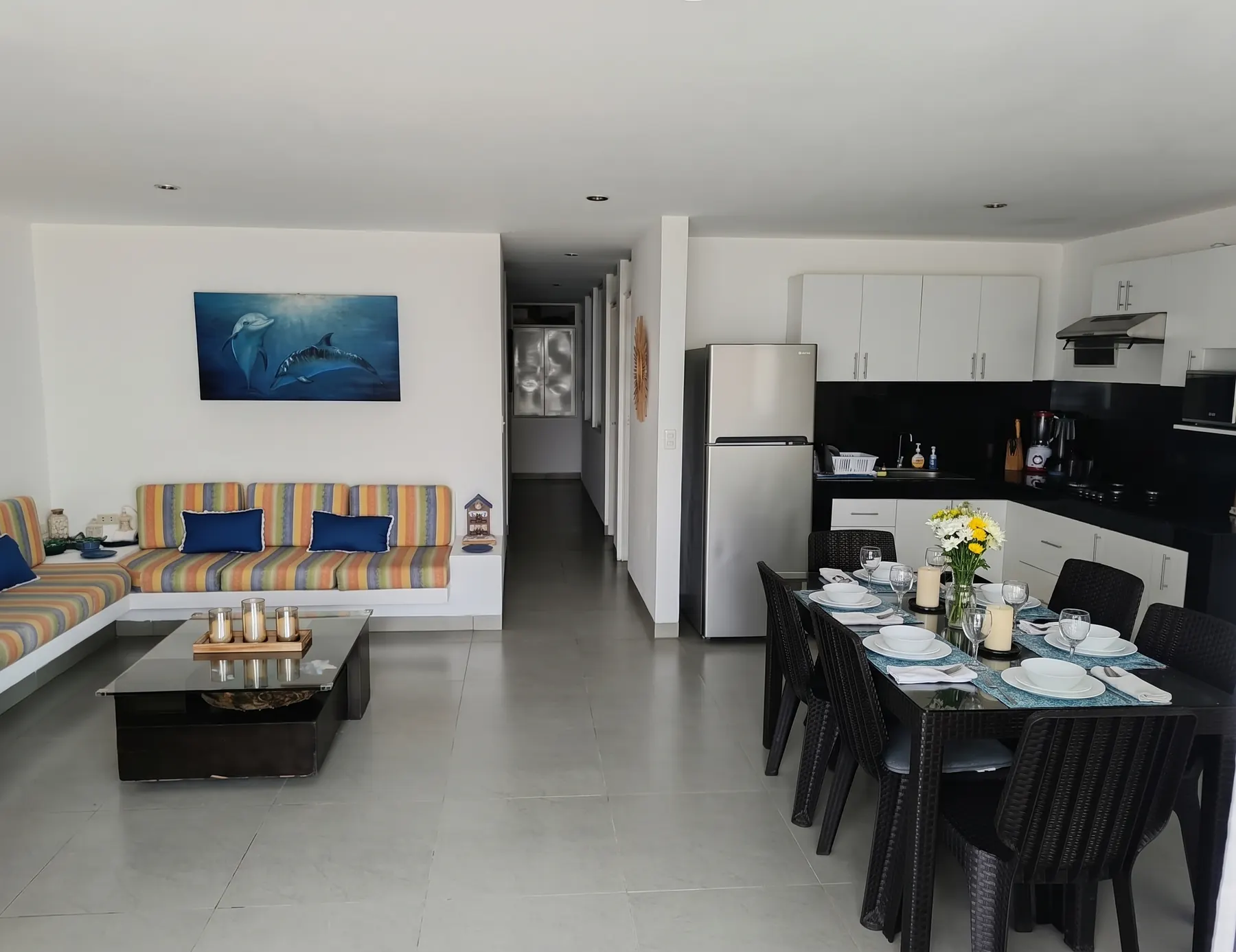 Sala y comedor abiertos: sofá en L con cojines a rayas, mesa de centro de vidrio y comedor para seis