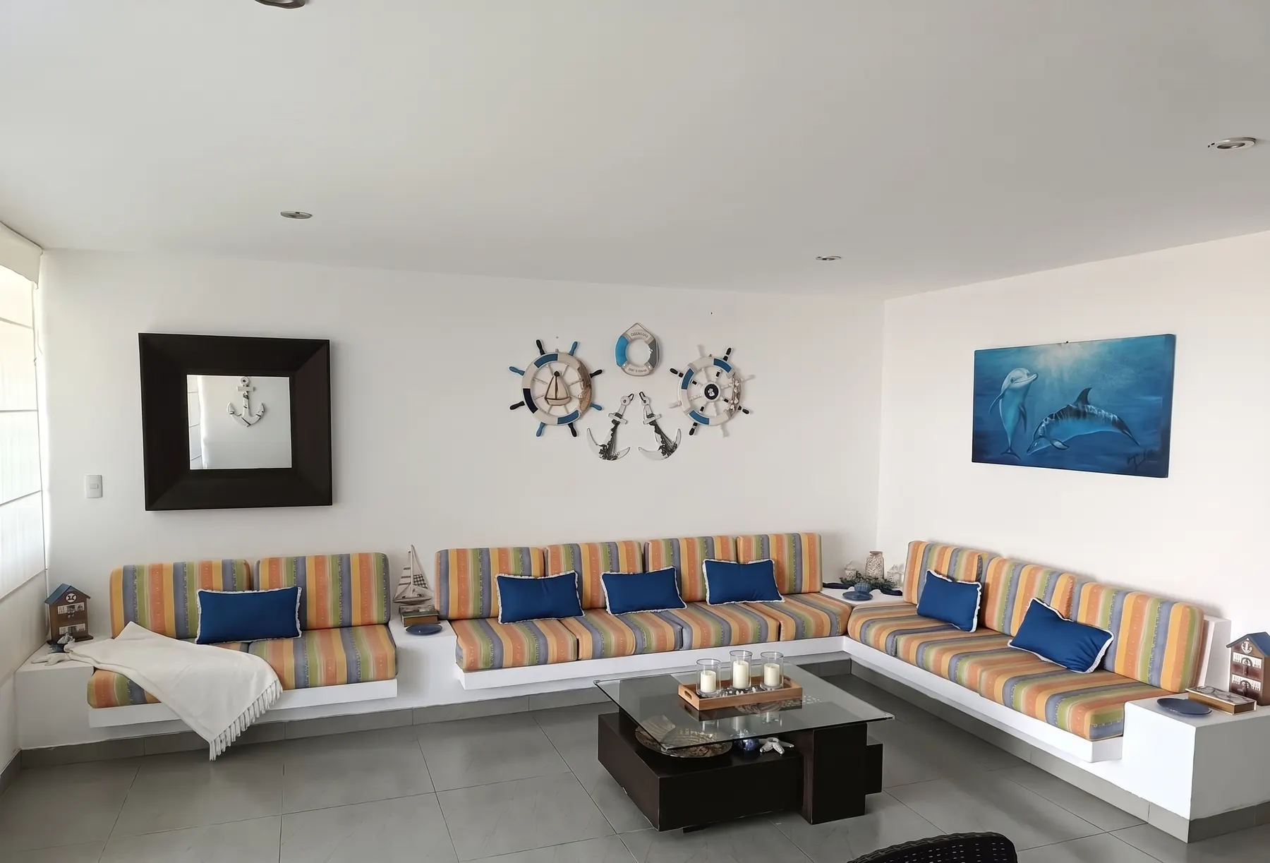 Sala con sofá empotrado en L, cojines a rayas, cojines azules y cuadros náuticos