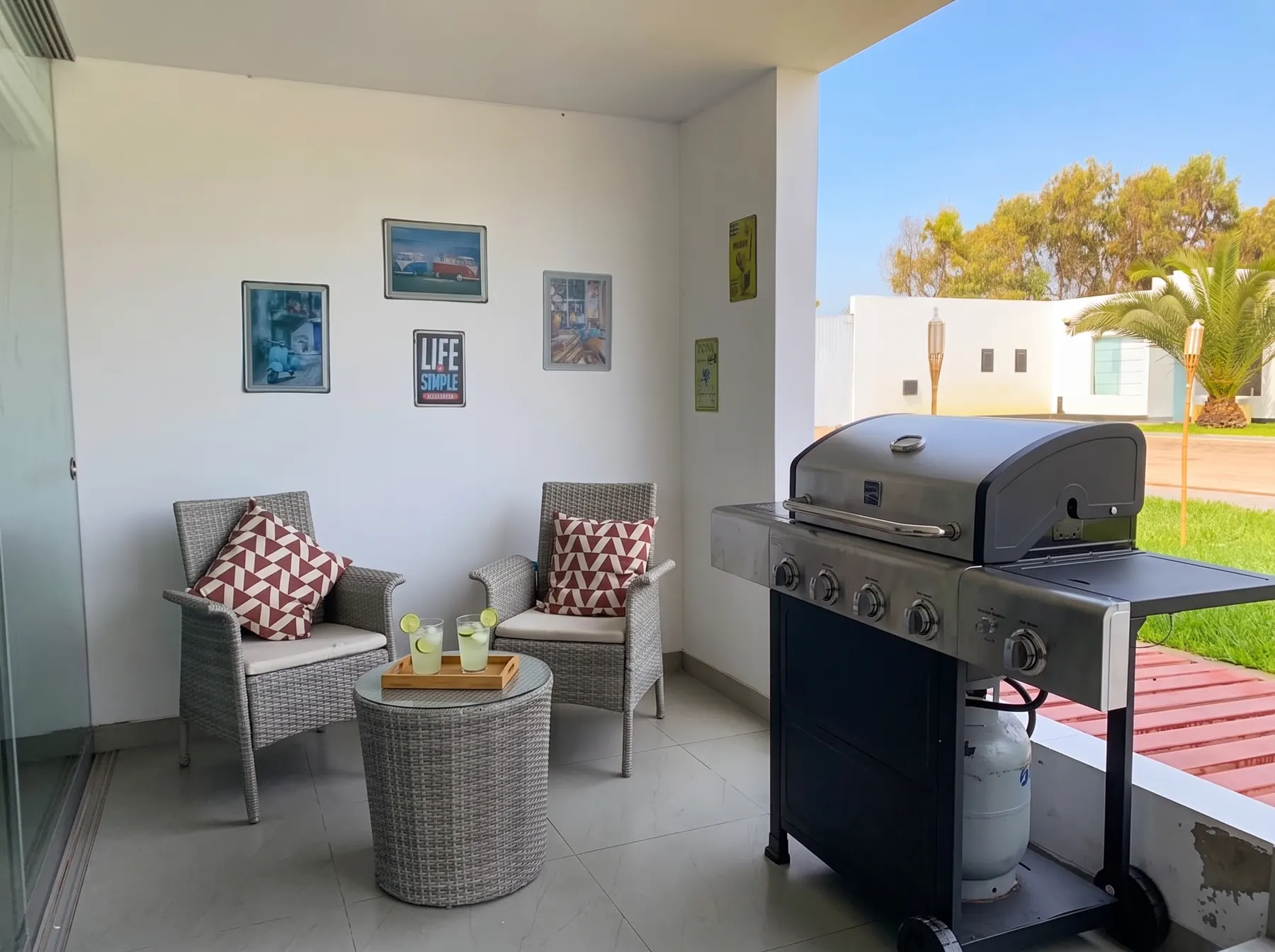 Terraza techada con dos sillones de mimbre, mesa auxiliar y parrilla a gas de acero